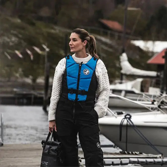 Lifestyle image of a female model wearing a Baltic Hera E.I. Buoyancy Aid in Aqua Blue while stood on a boat pontoon.